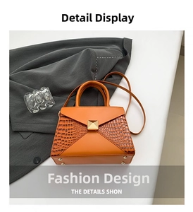 Close-up of crocodile embossed texture and gold pyramid rivet on orange-brown handbag