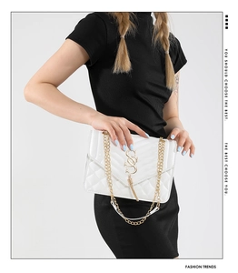 Close-up of white quilted envelope bag with gold S-logo, tassel and metal chain strap