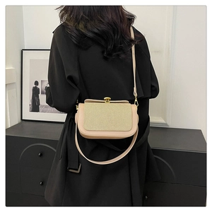 Détail d'un sac bandoulière crème avec texture tressée et fermoir doré sur manteau noir