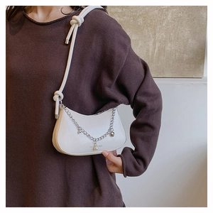 Detail of white half-moon shoulder bag with pearl charms and metal chains worn by model