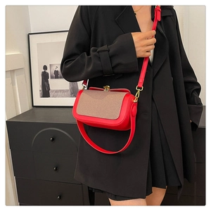 Détail du sac à bandoulière en cuir rouge avec rabat tissé marron et boucle dorée chic