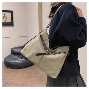 Detail view of khaki canvas tote bag with brown leather straps and gold buckle accents