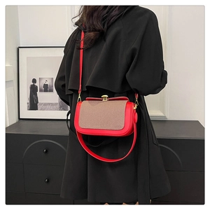 Détail du sac bandoulière en cuir rouge avec rabat tissé et fermoir doré sur un manteau noir