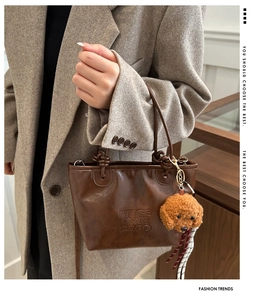 Detail of brown leather bucket bag with brand embossing and plush poodle charm