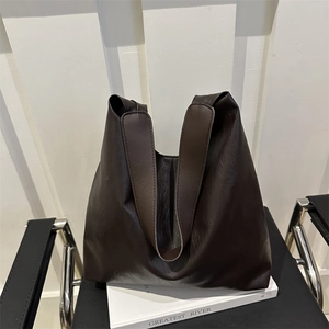 Minimalist dark brown leather tote bag displayed on a sleek black bench in a modern room