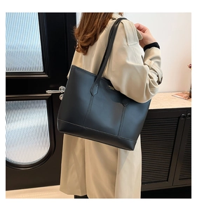 Detailansicht der schwarzen matten Ledertote mit Goldlogo auf einem lässigen Trenchcoat