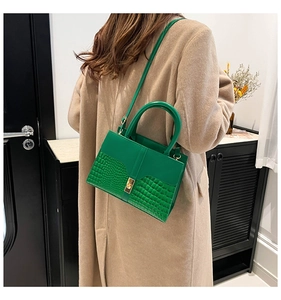 Detail of green tote bag with crocodile pattern and golden metal lock on wool coat