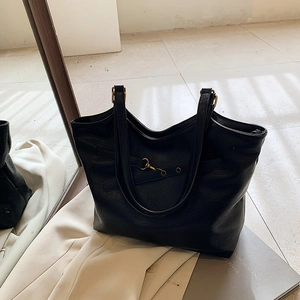 Vintage black leather tote bag with gold metal buckle shown on a magazine background