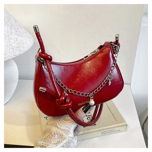 Detail of red crescent bag with glossy leather texture, silver chains and star charms