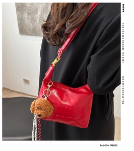 Detail of red glossy leather tote bag with embossed logo and plush teddy bear charm