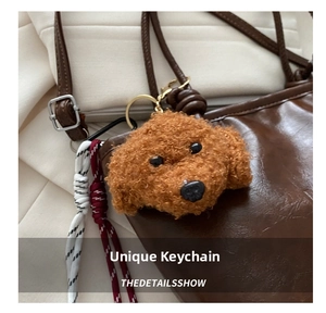 Detail of a brown plush poodle charm with a gold metal clasp on a leather handbag