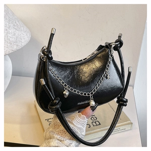 Detail of black faux leather crescent bag with silver chain and heart pearl charm