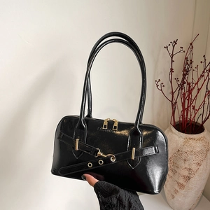 Glossy black bowling handbag with gold hardware and fashion embossing held by hand