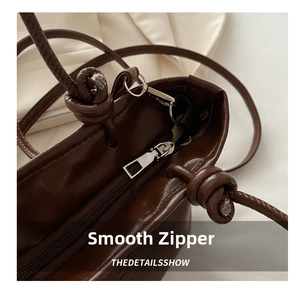 Close-up of a silver zipper and knotted handle on a vintage brown leather bucket bag