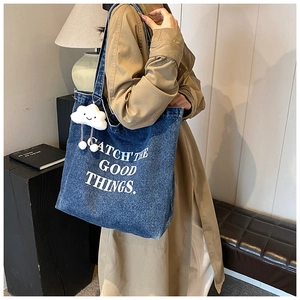 Détail du sac cabas en jean bleu avec texte blanc et pendentif en forme de nuage doux