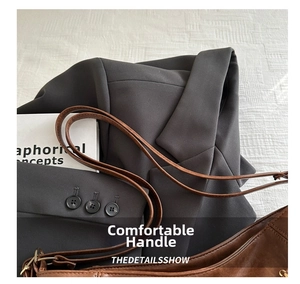 Detail of retro dark brown textured leather tote bag on a gray suit sleeve background