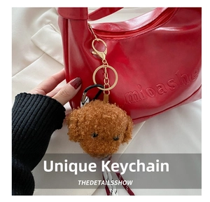 Detailed view of a brown curly plush teddy dog charm on a red leather tote bag