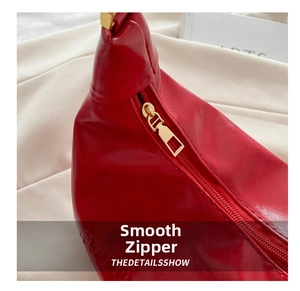 Close-up of a premium gold metal zipper on a textured red leather crossbody bag detail
