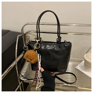Detail of black PU tote bag with plush bear charm and woven rope on a metal rack