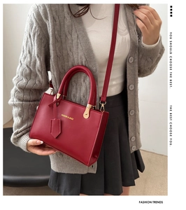 Detail showing deep red leather handbag with gold embossed text and metallic hardware