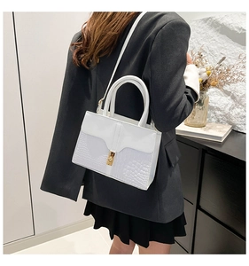 Detail view of white crocodile pattern leather handbag with gold twist lock closure