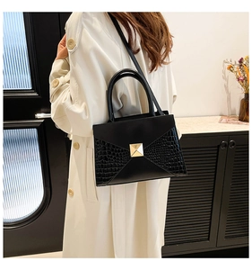 Modern black拼接 handbag with crocodile texture and gold lock shown on model indoors
