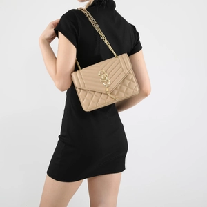 Detail of nude quilted crossbody bag with golden chain strap and tassel on a model
