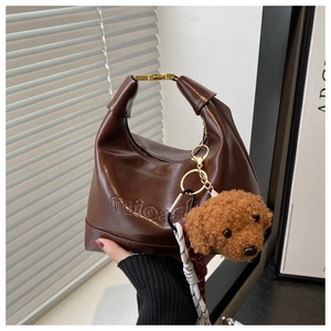 Detail of a brown leather tote bag featuring mioash embossing and a cute teddy charm