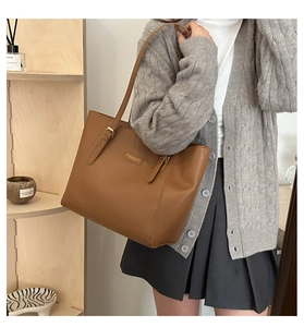 Brown leather tote bag featuring golden hardware and decorative buckle straps on model