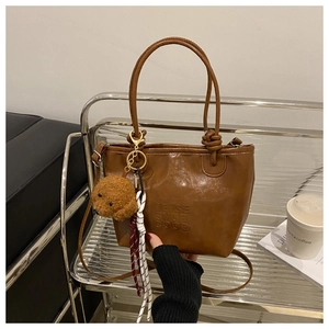 Close-up of brown faux leather tote with NEIGE SNUR GOOD embossed text and teddy charm
