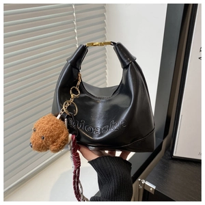 Detail of black hobo bag with teddy charm, gold clasp, and nioashe embossed logo