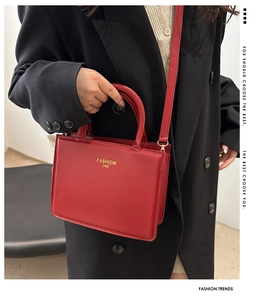 Detail of red patent leather square handbag with gold FASHION BAG text on black coat