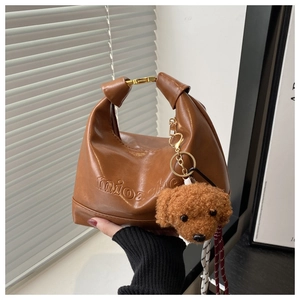 Close-up of brown faux leather handbag featuring embossed brand text and a cute dog pendant
