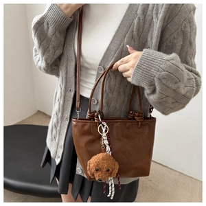 Detail of a brown trapezoid handbag with a teddy bear charm and striped ribbon on strap