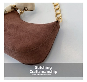 Dettaglio borsa a spalla in camoscio marrone con catena dorata e accessorio foulard