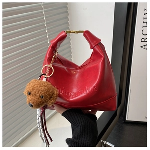 Detail of red vintage handbag featuring gold metal buckle and brown teddy bear charm