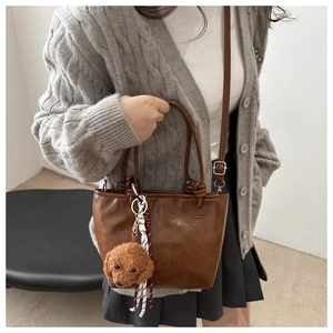 Detail of vintage brown leather tote bag with plush dog charm and woven strap accents
