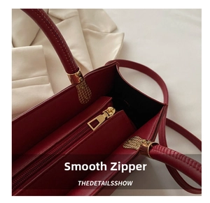Close-up of wine red leather tote bag showing golden metal zipper and handle details