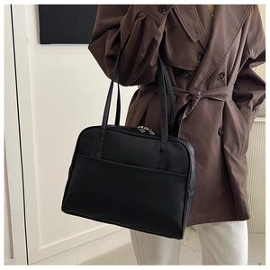 Détail d'un grand sac cabas en cuir noir avec zip doré porté avec un trench-coat marron