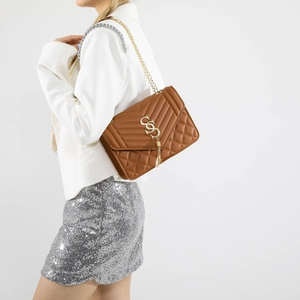 Brown quilted shoulder bag with gold chain strap and fringe tassel on elegant model