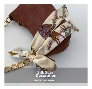 Dettaglio borsa a mezzaluna in camoscio marrone con catena dorata e foulard di seta chic
