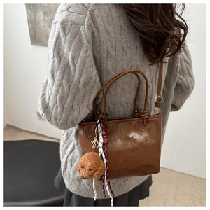 Detail view of a vintage brown leather bucket bag with teddy bear charm and embossed text