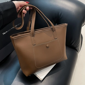 Borsa tote minimalista in pelle marrone con tasca frontale su sfondo di pelle nera