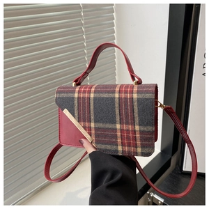 Detail of red leather handle and gold metal trim on a vintage plaid crossbody bag