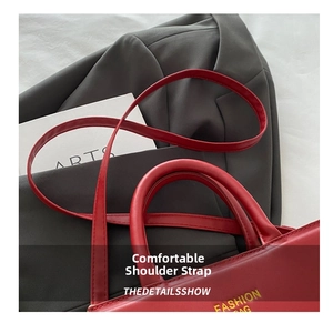 Detail view of red leather shoulder bag with gold engraving on a tailored grey suit jacket