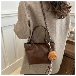 Close-up of vintage brown leather bucket bag with embossed logo and plush dog charm