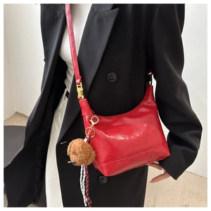 Detail of red faux leather handbag with embossed text and brown teddy bear charm