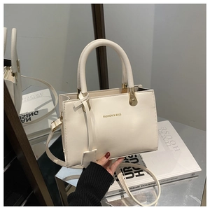 Detail view of cream white tote bag with gold hardware and logo on a silver platform