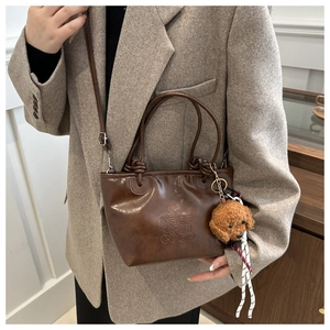 Detail of vintage brown leather bucket bag with teddy bear charm on grey wool coat