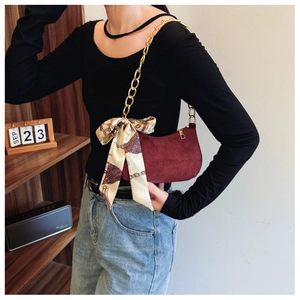 Detail of burgundy suede moon bag with chunky gold chain and decorative silk scarf